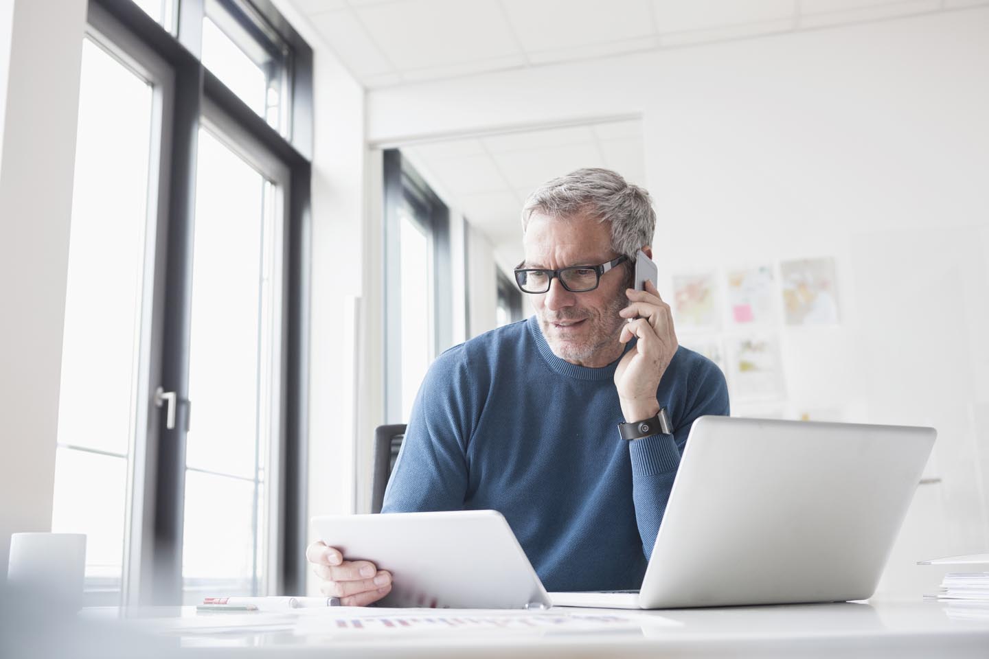 Ein Mann mit Brille sitzt im Büro an seinem Laptop und telefoniert.