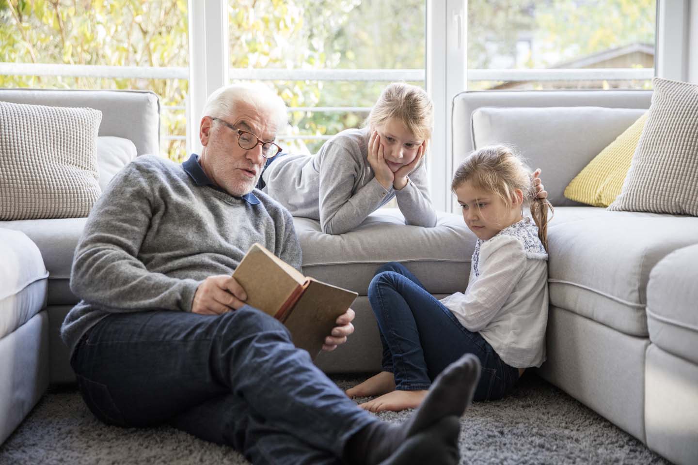 Ein Großvater liest seinen Enkelinnen aus einem Buch vor.