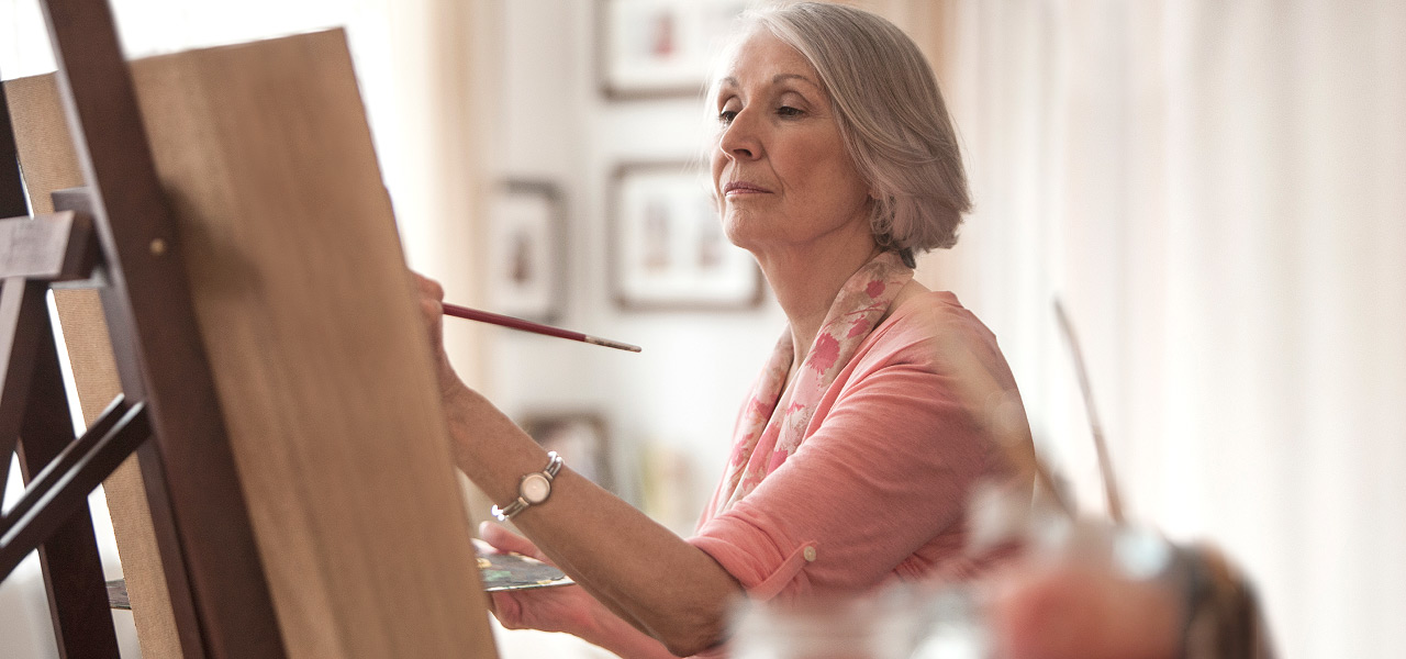 Ältere Frau malt auf einer Leinwand.