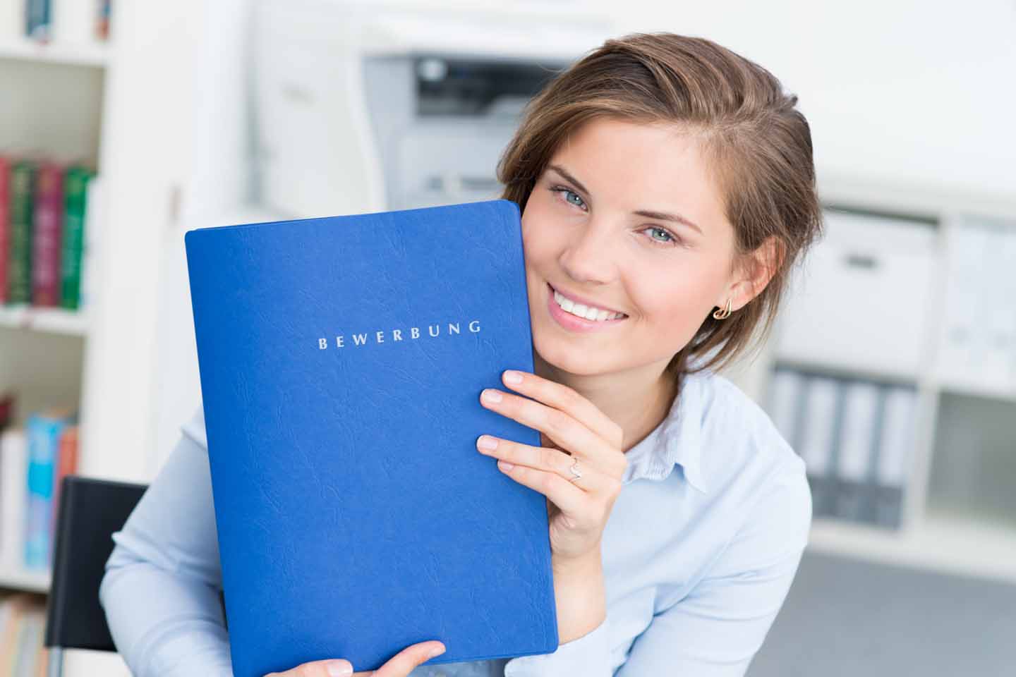 Eine eine junge Frau zeigt auf eine blaue Bewerbungsmappe.