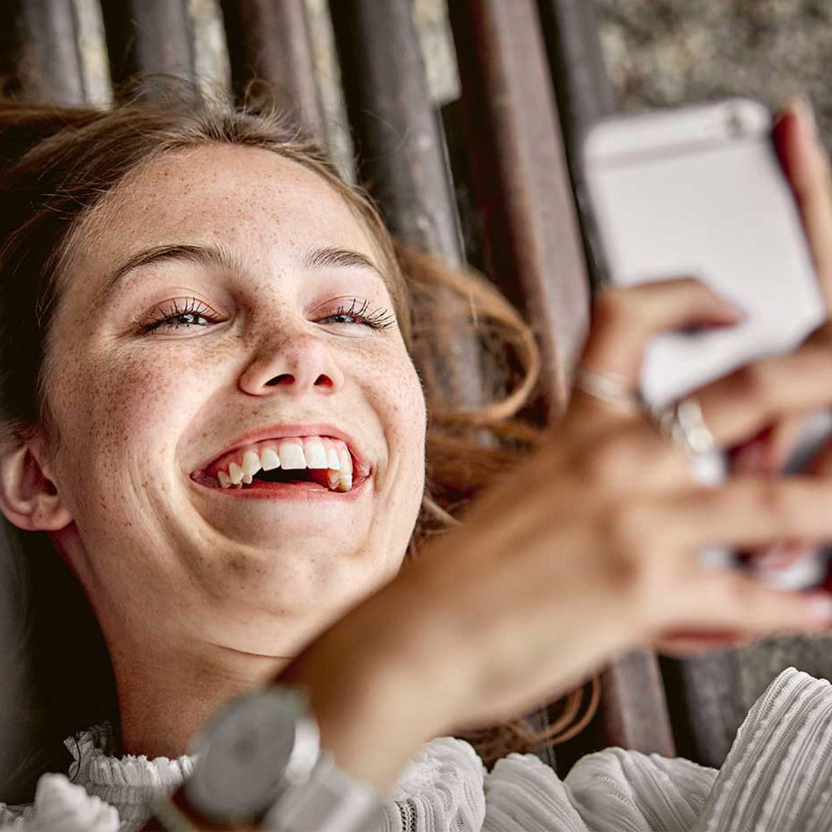 Eine junge Frau schaut lachend auf ihr Smartphone, dabei sieht man ihre schönen Zähne.