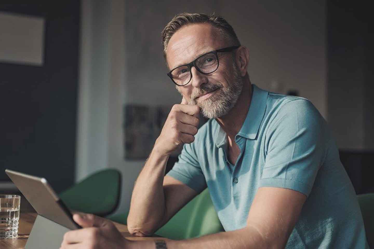 Ein Mann sitzt am Tisch, das Surface aufgeklappt und lächelt in die Kamera.