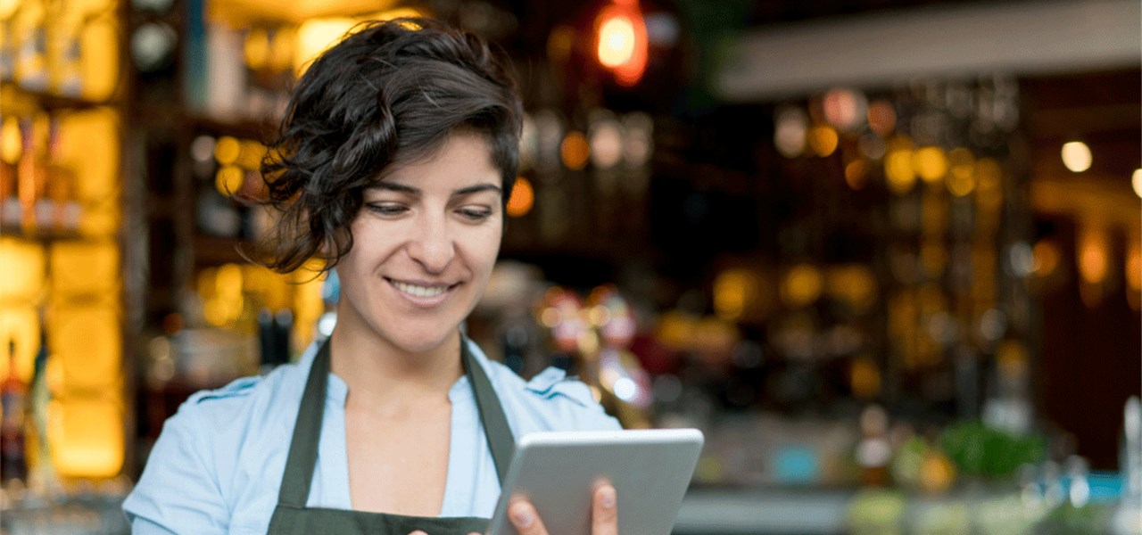 Eine Frau mit Schürze sieht auf ein Tablet. 