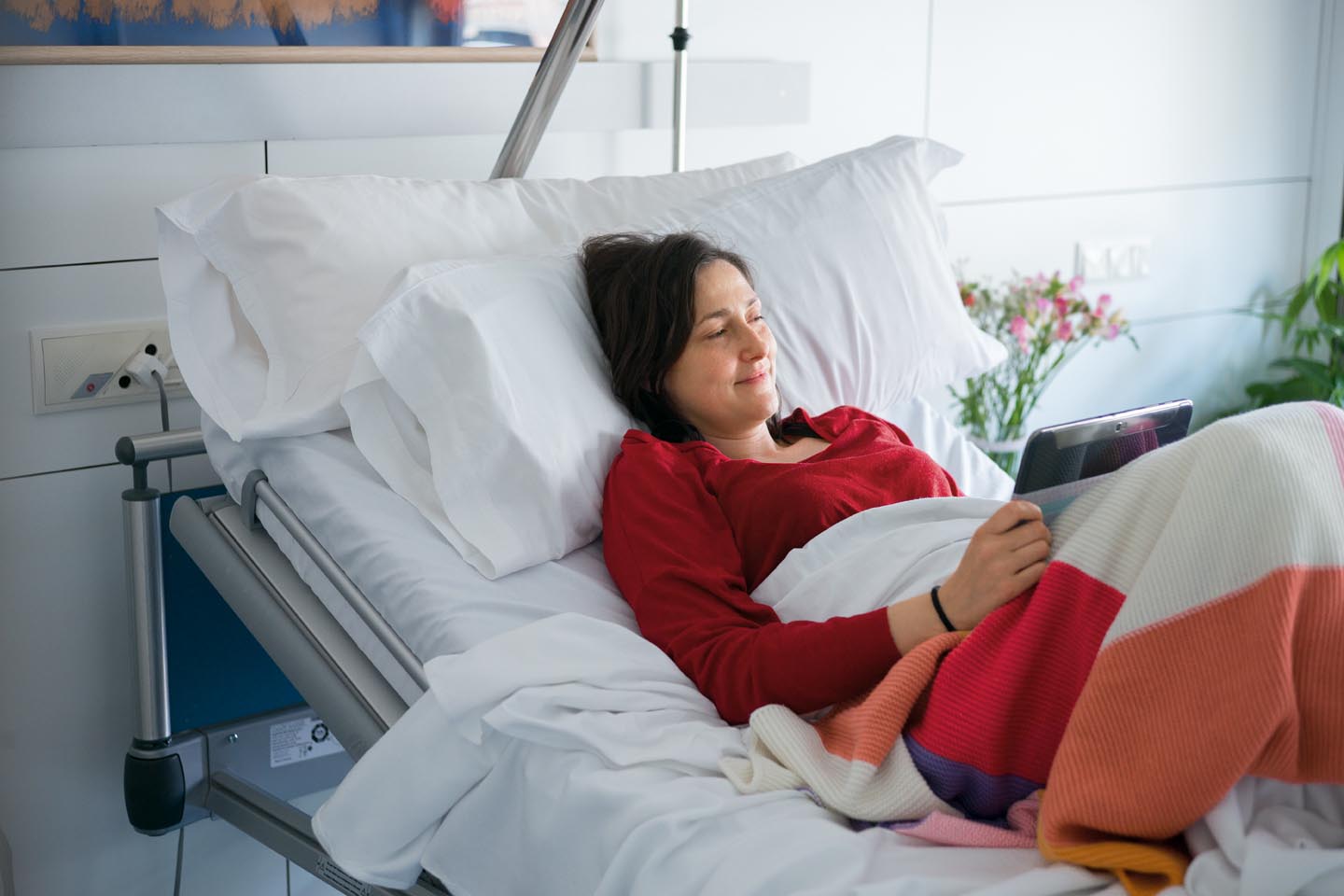 Frau liegt im Krankenhausbett und schaut aufs Tablet