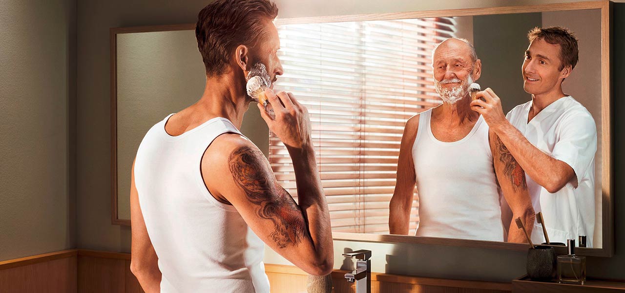 Mann beim Rasieren schaut in den Spiegel.