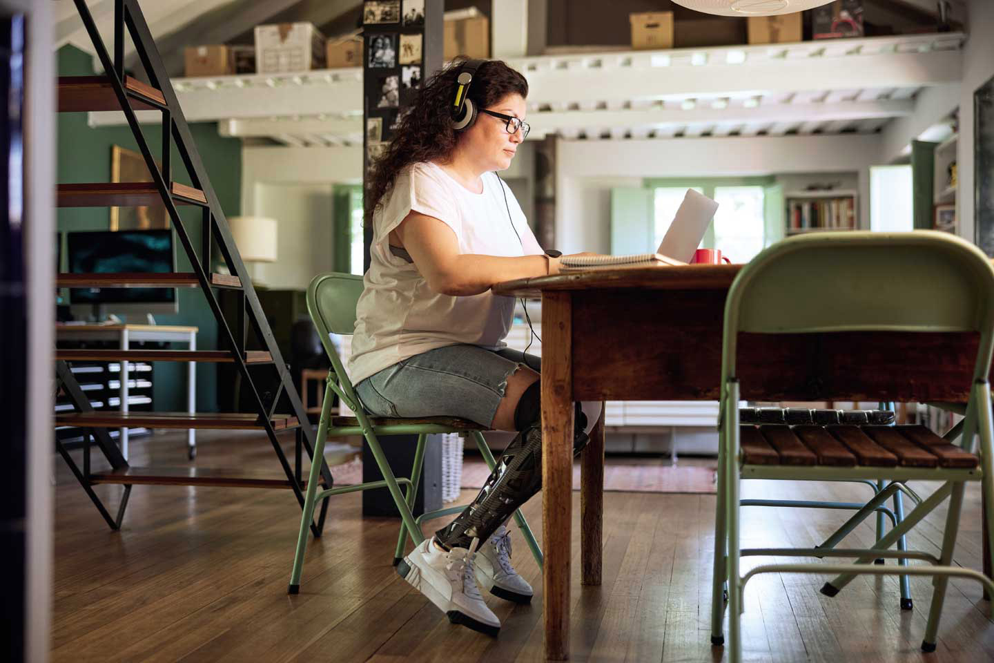 Eine Frau mit Beinprothese sitz am Laptop und arbeitet von zuhause. 