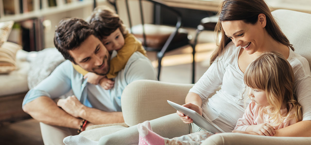 Junge Familie mit zwei Kindern sitzt zusammen im Wohnzimmer.