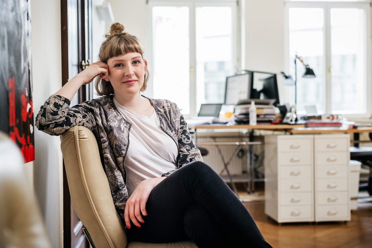 Porträt einer jungen, lässigen Start-up-Geschäftsfrau in ihrem Büro. Sie sitzt auf einem Stuhl und lächelt in die Kamera.