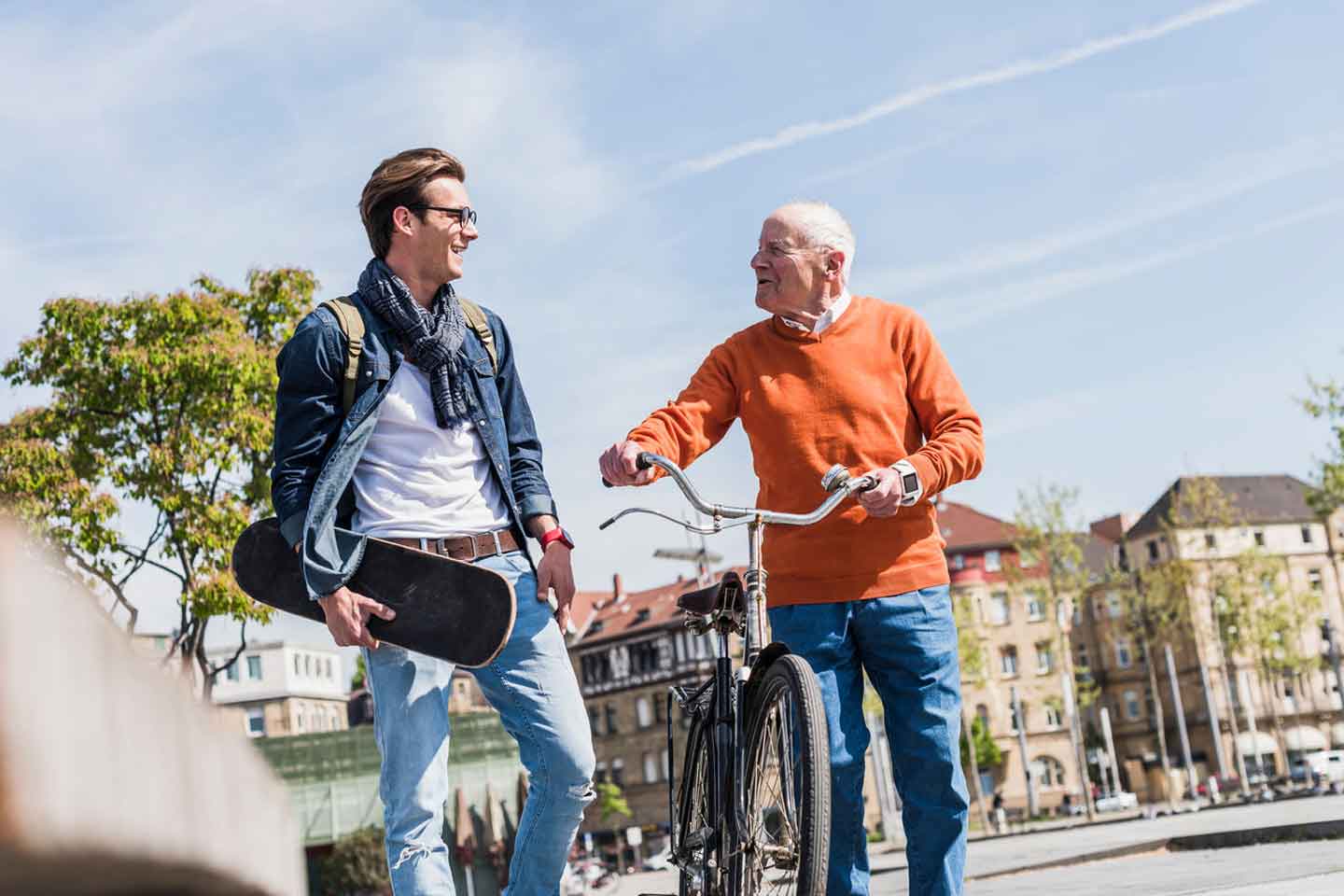 Älterer Mann mit Fahrrad unterhält sich angeregt mit jüngerem Mann, der ein Skateboard trägt.