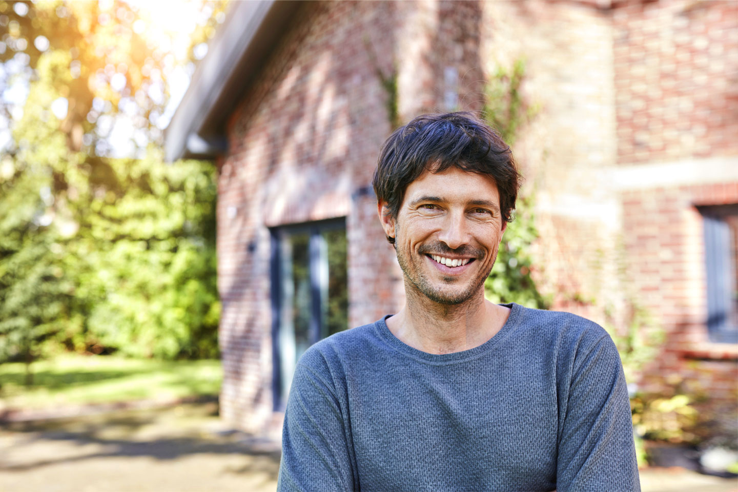 Ein Mann steht vor einem Haus und lächelt in die Kamera. 