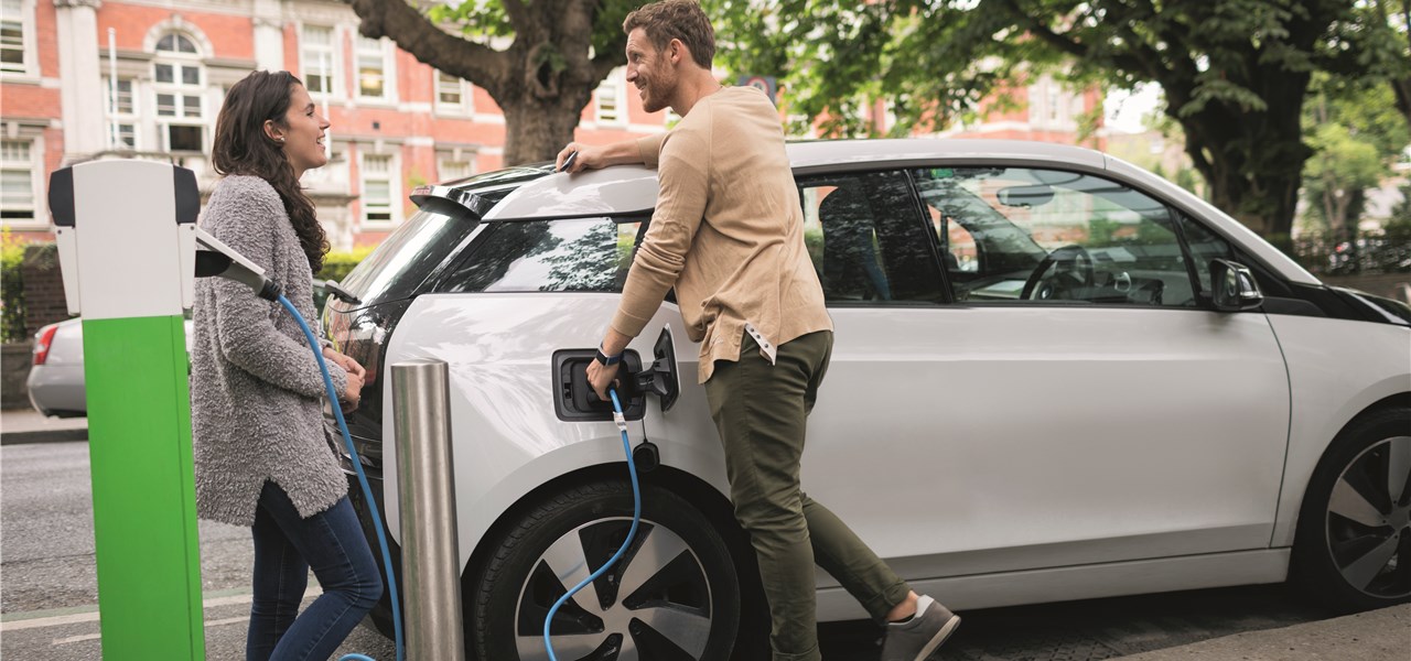 An einer E-Ladestation quatscht ein Pärchen am Auto lehnend.