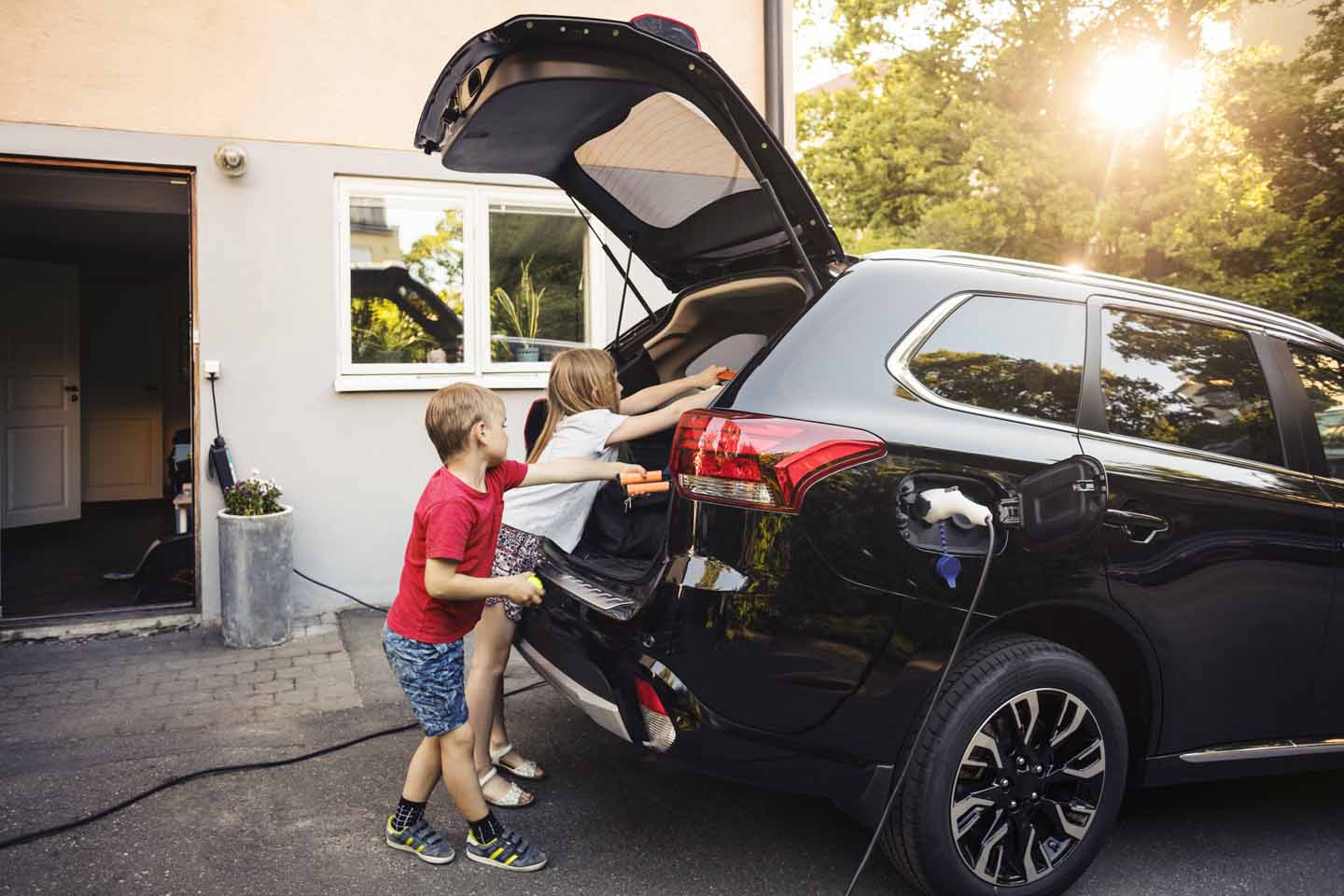 Kinder am Kofferraum eines schwarzen Autos.