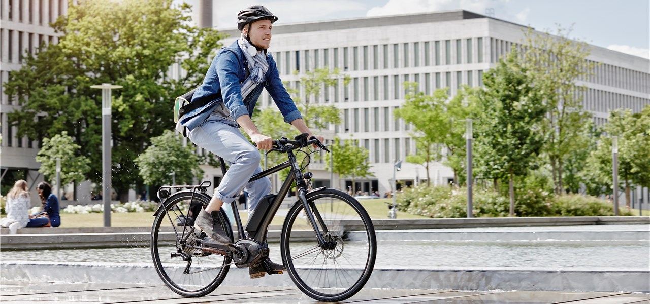 Ein Mann in Businesskleidung fährt mit dem E-Bike durch die Stadt.