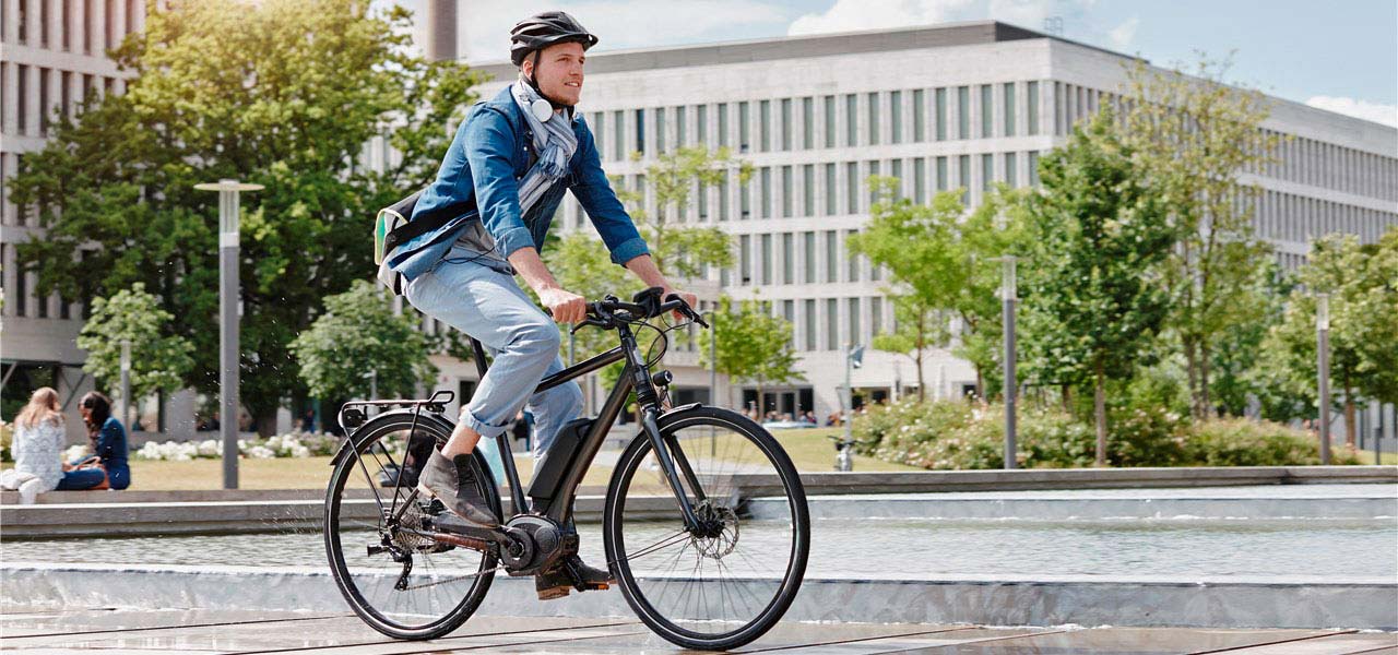 Ein Mann in Businesskleidung fährt mit dem E-Bike durch die Stadt.