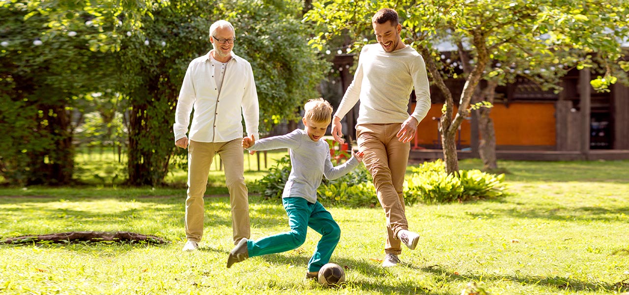 3 Generationen von Männern spielen im Garten Fußball: Ein Opa, der Sohn und der Enkel.