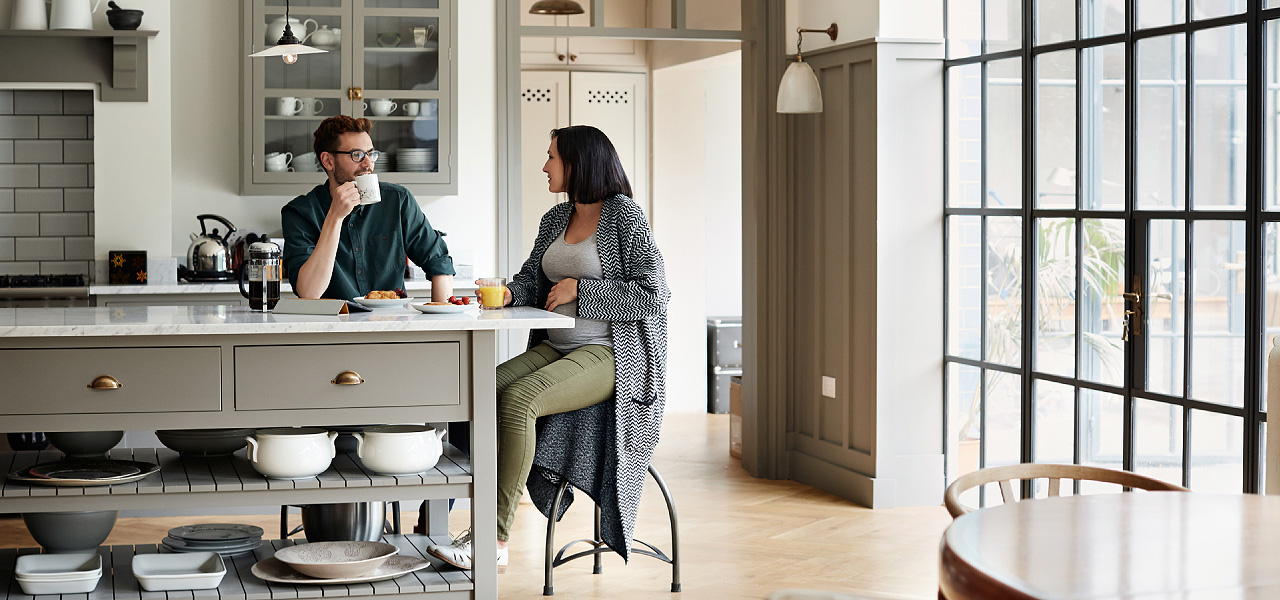 Eine schwangere Frau und ein Man  sitzen in einer Küche und frühstücken. 