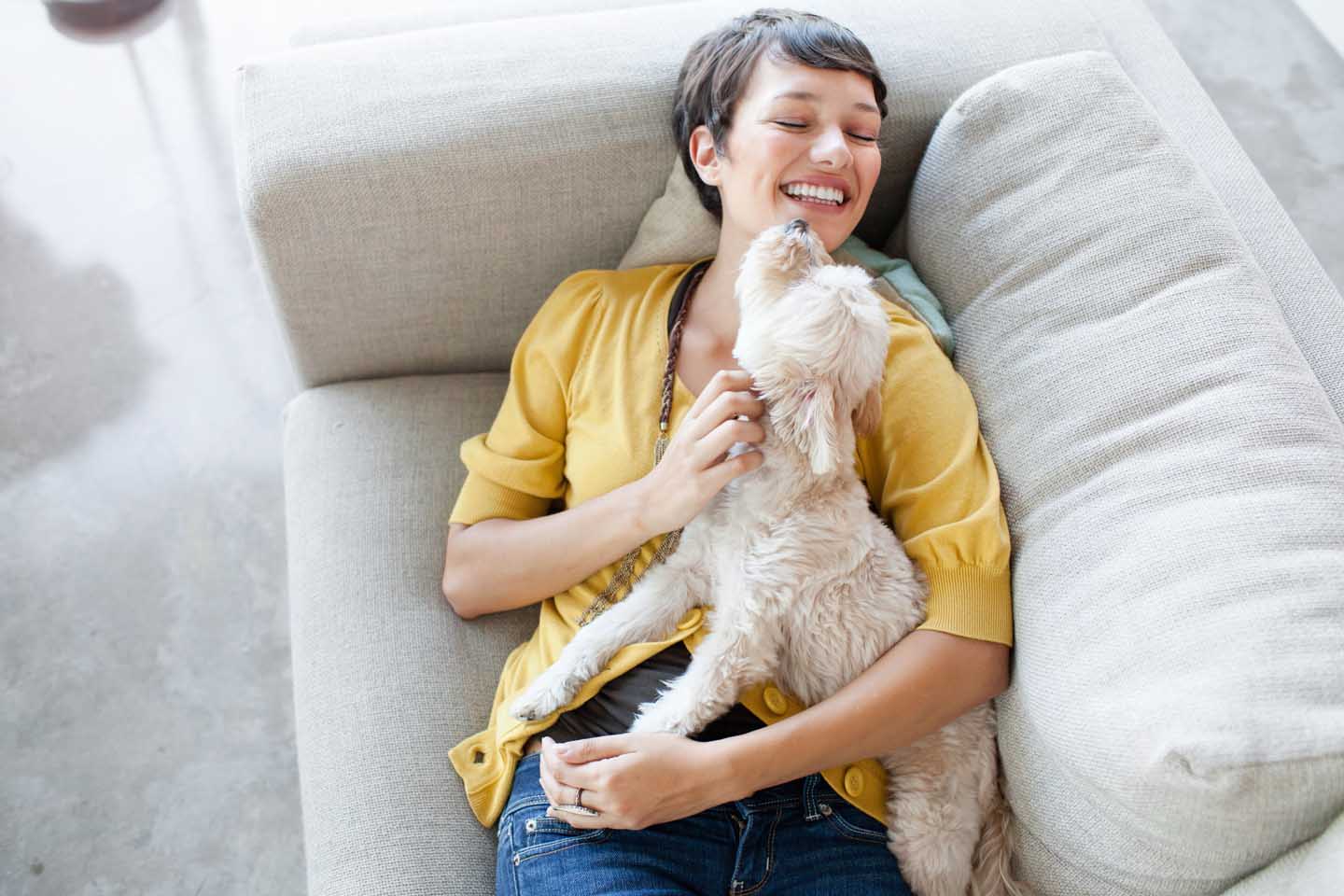 Eine Frau schmust auf dem Sofa mit einem Hund. 