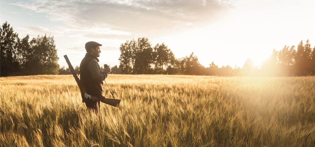 Ein Jäger steht in einem Weizenfeld. Er hat ein Gewehr um die Schultern.