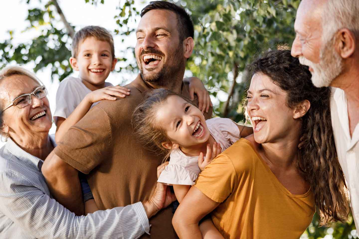 Drei Generationen – Großeltern, Eltern und Kind – gehen lachend am Strand spazieren.