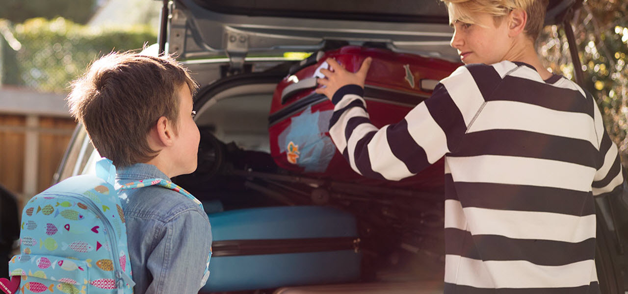 Junge Mutter packt den Kofferraum eines Autos, es geht in den Urlaub.