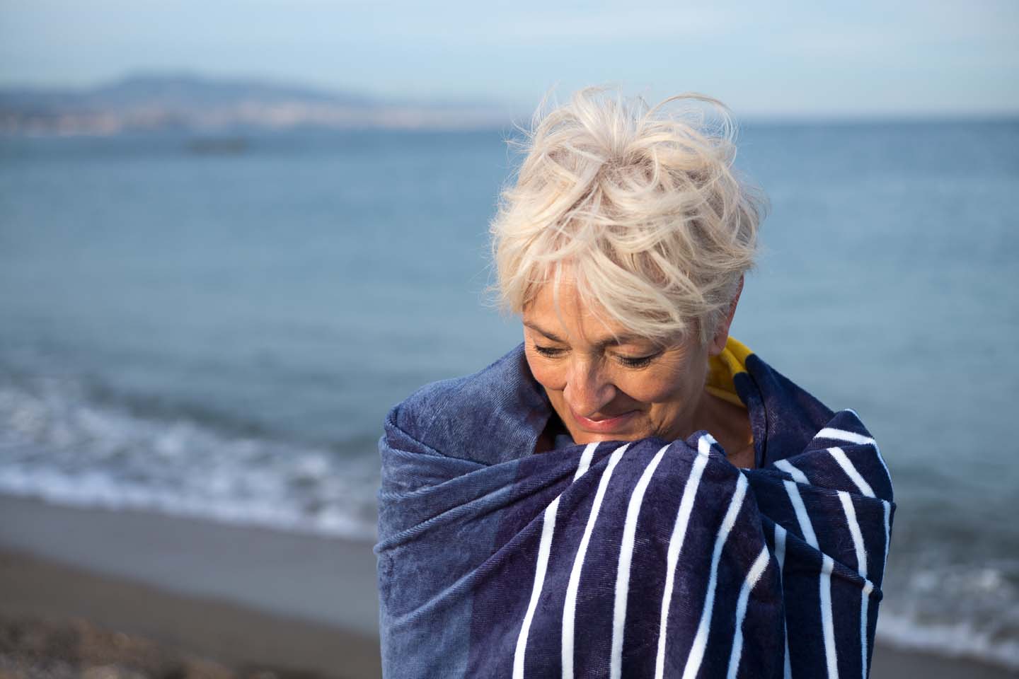 Ältere Dame mit Handtuch am Strand.