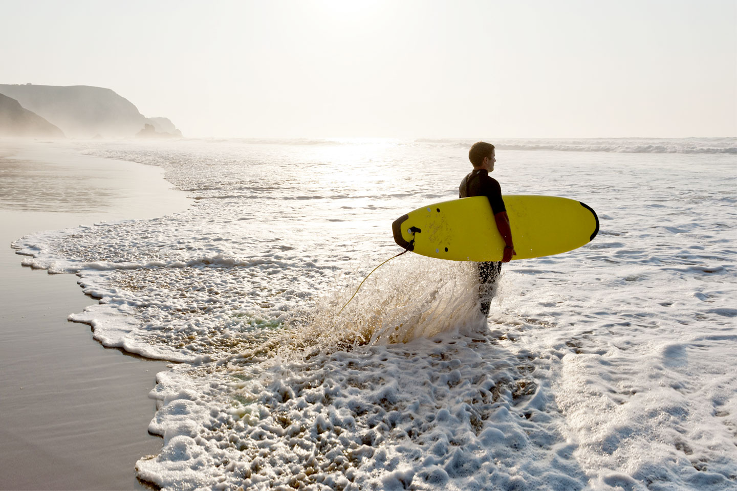 Junger Mann geht mit seinem Surfbrett ins Meer.