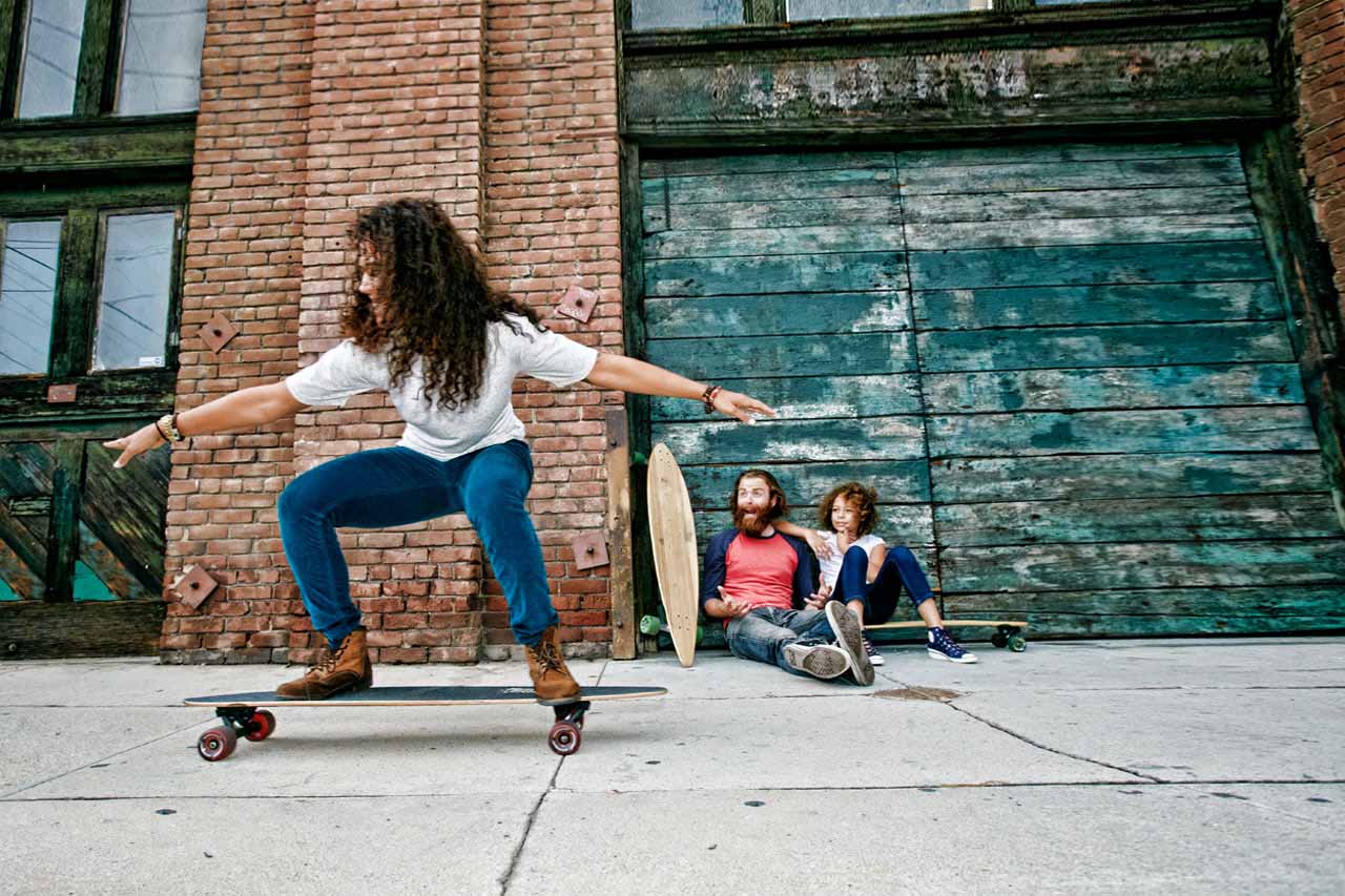 Eine Frau fährt Skateboard, während ein Mädchen und ein Mann begeistert zuschauen.