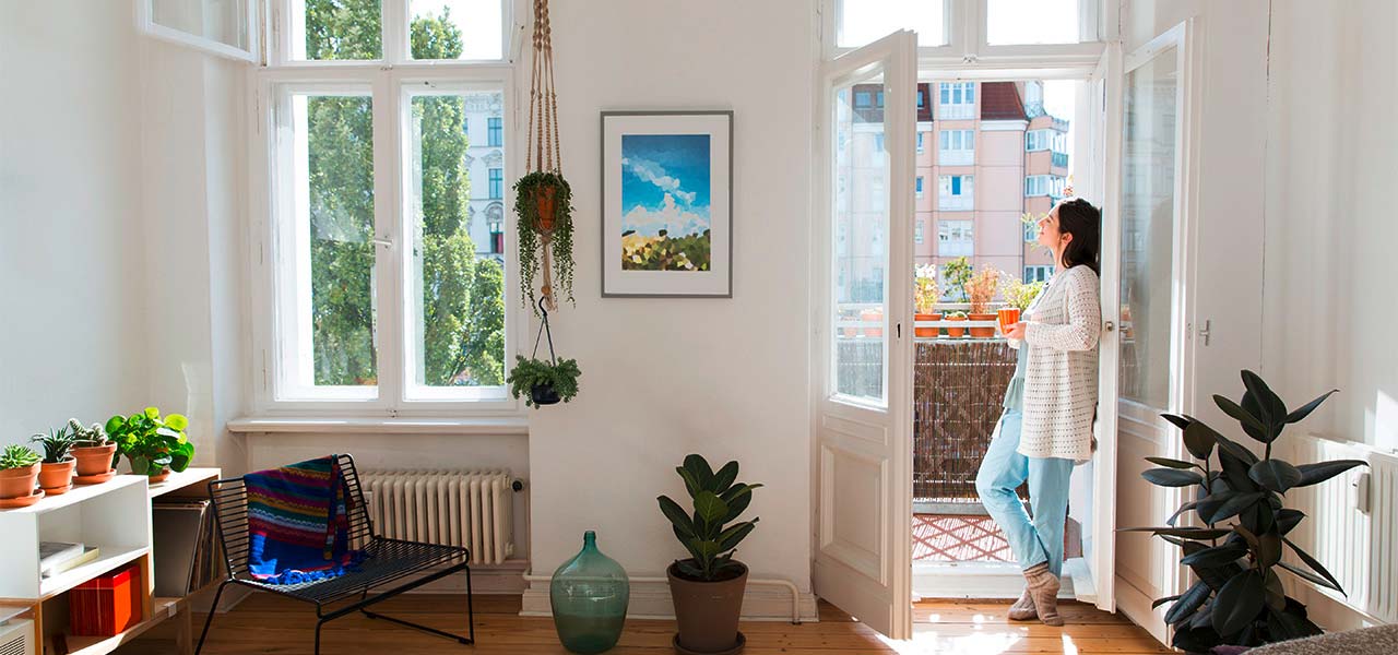 In einem modern eingerichteten Altbau steht eine Frau mit Tasse an der doppelflügligen Balkontür.