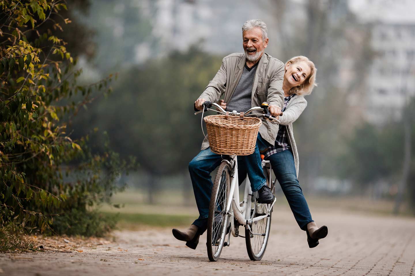 Ein lachendes älteres Paar zusammen auf einem Fahrrad – der Mann fährt, die Frau sitzt auf dem Gepäckträger.