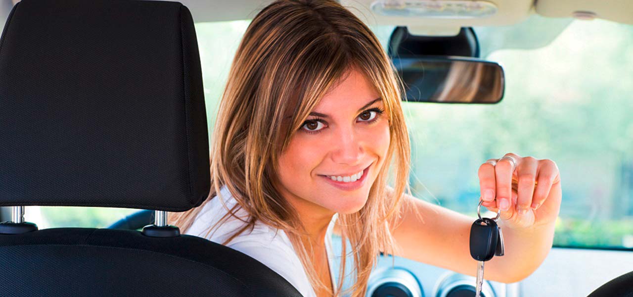 Eine Frau zeigt stolz in ihrem Auto sitzend die Schlüssel.