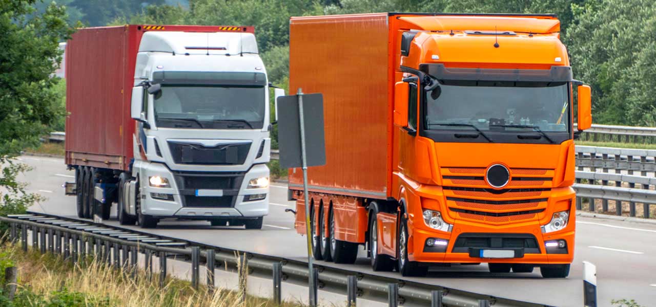 Zwei LKW fahren auf einer gut ausgebauten Straße hintereinander her.