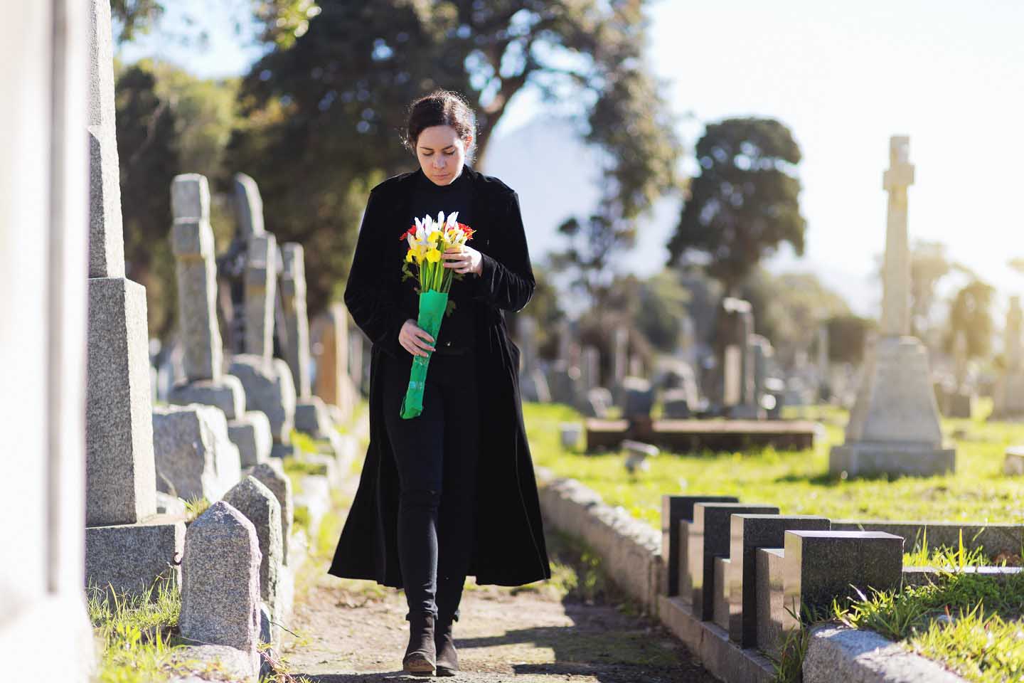 Eine junge Frau geht traurig über den Friedhof. 