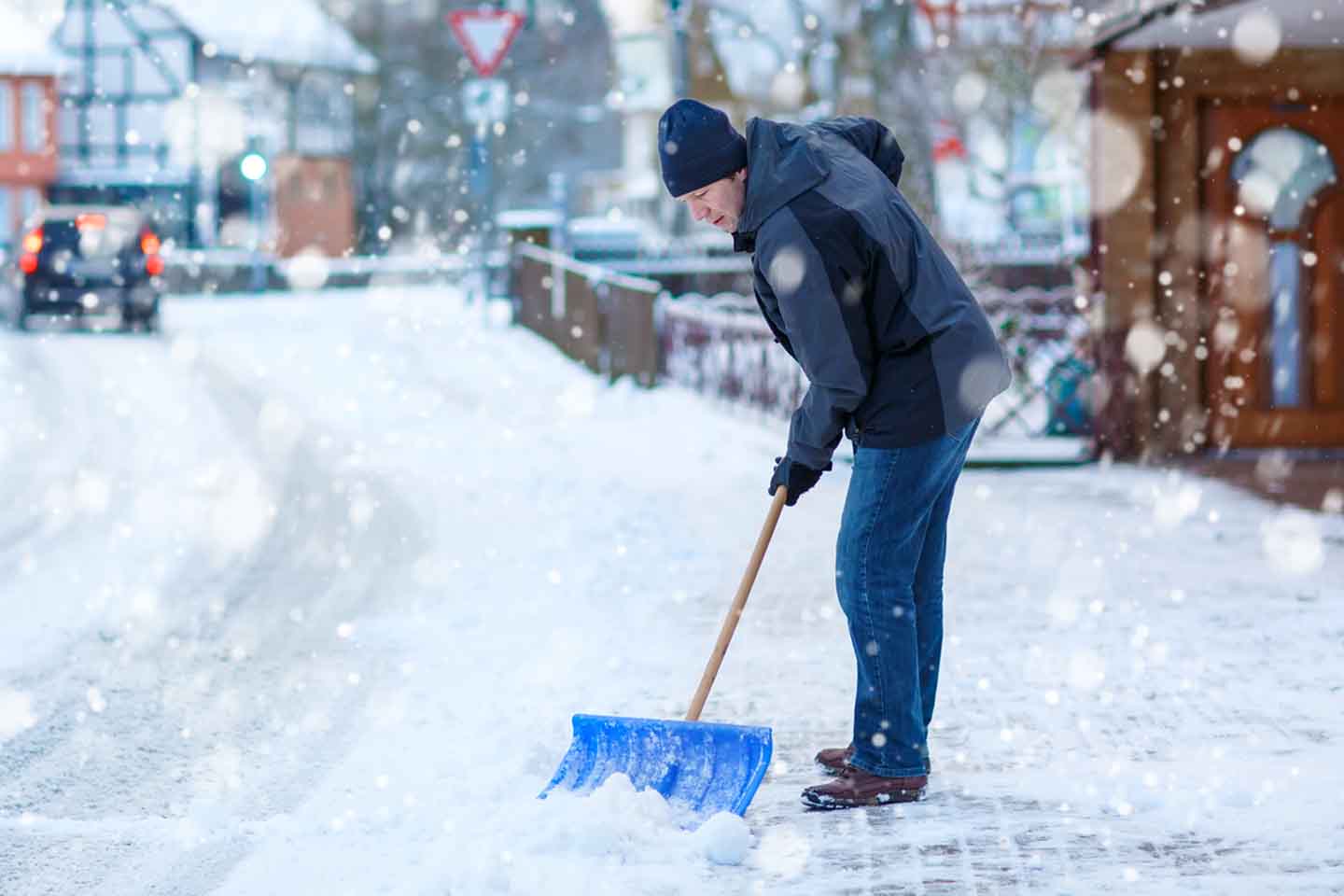 Ein Mann mit Schneeschaufel reinigt den Gehweg.