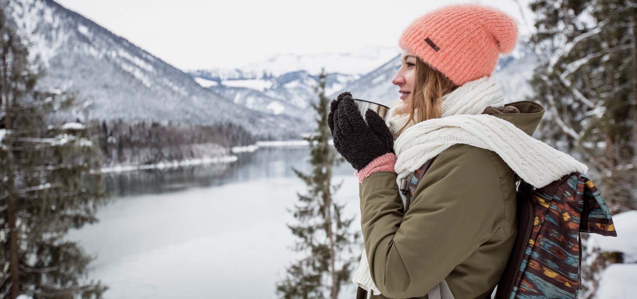 Beim Wandern: Eine Frau trinkt eine heiße Tasse Tee an einem verschneiten Wintersee.
