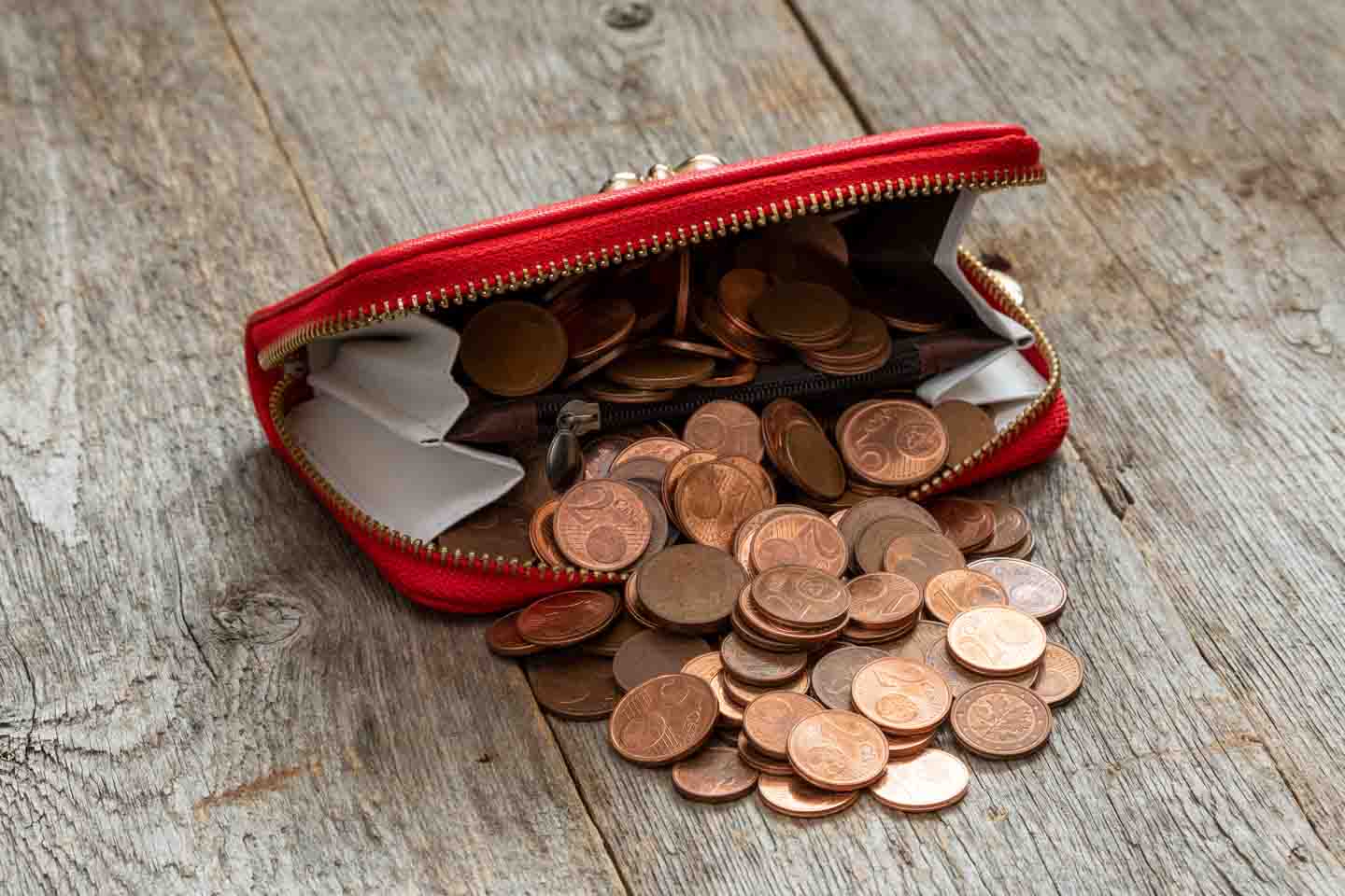 Kupfergeld quillt aus einem roten Geldbeutel, der auf einem Holztisch liegt.