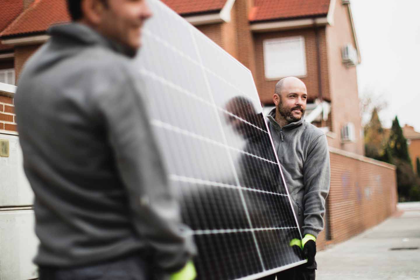 Zwei Experten tragen Solarpanele vor einem Haus.