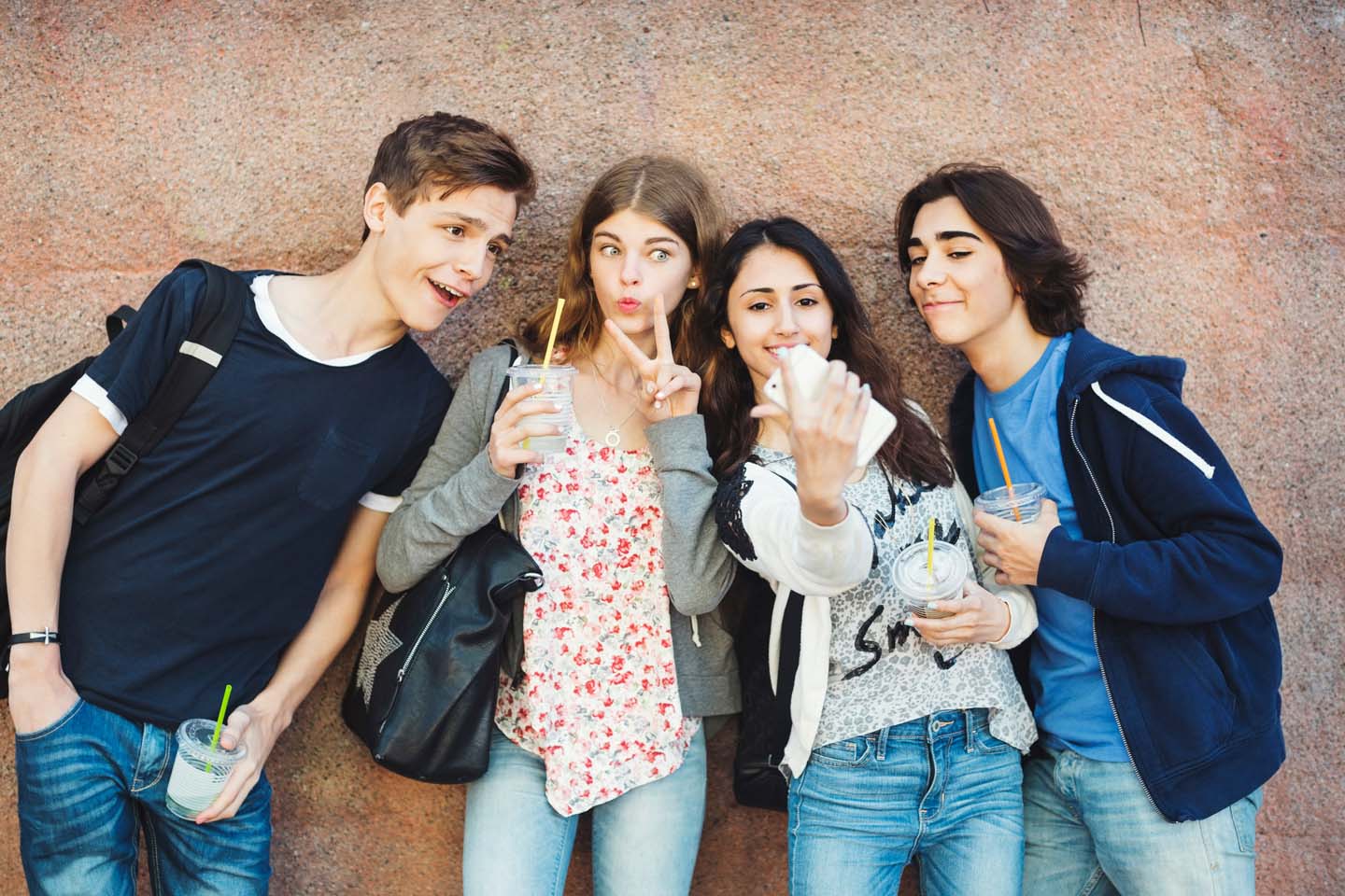 Happy teenagers gesturing while taking selfie against wall