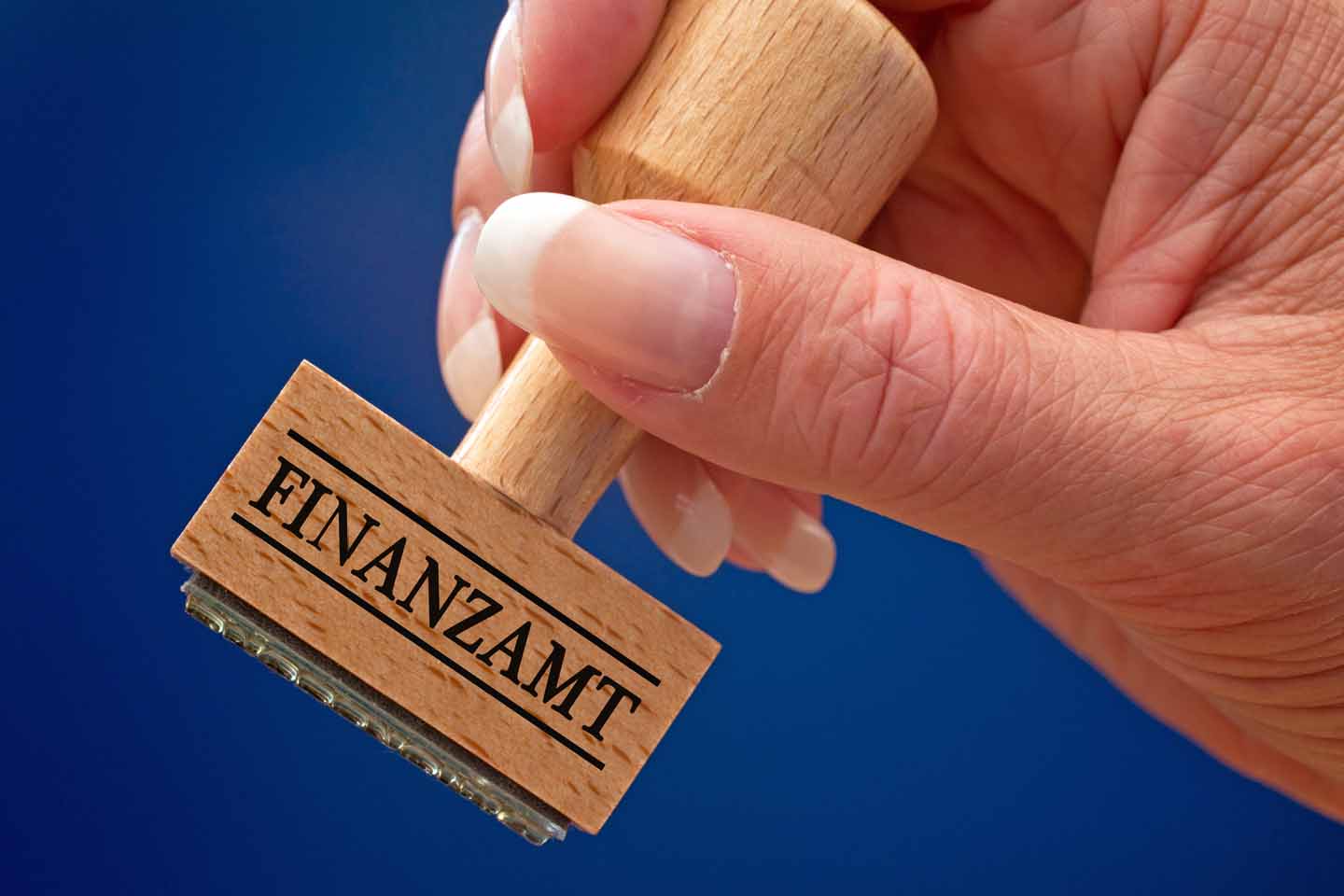 Eine Hand hält einen Stempel mit der Aufschrift: "Finanzamt" in die Kamera.
