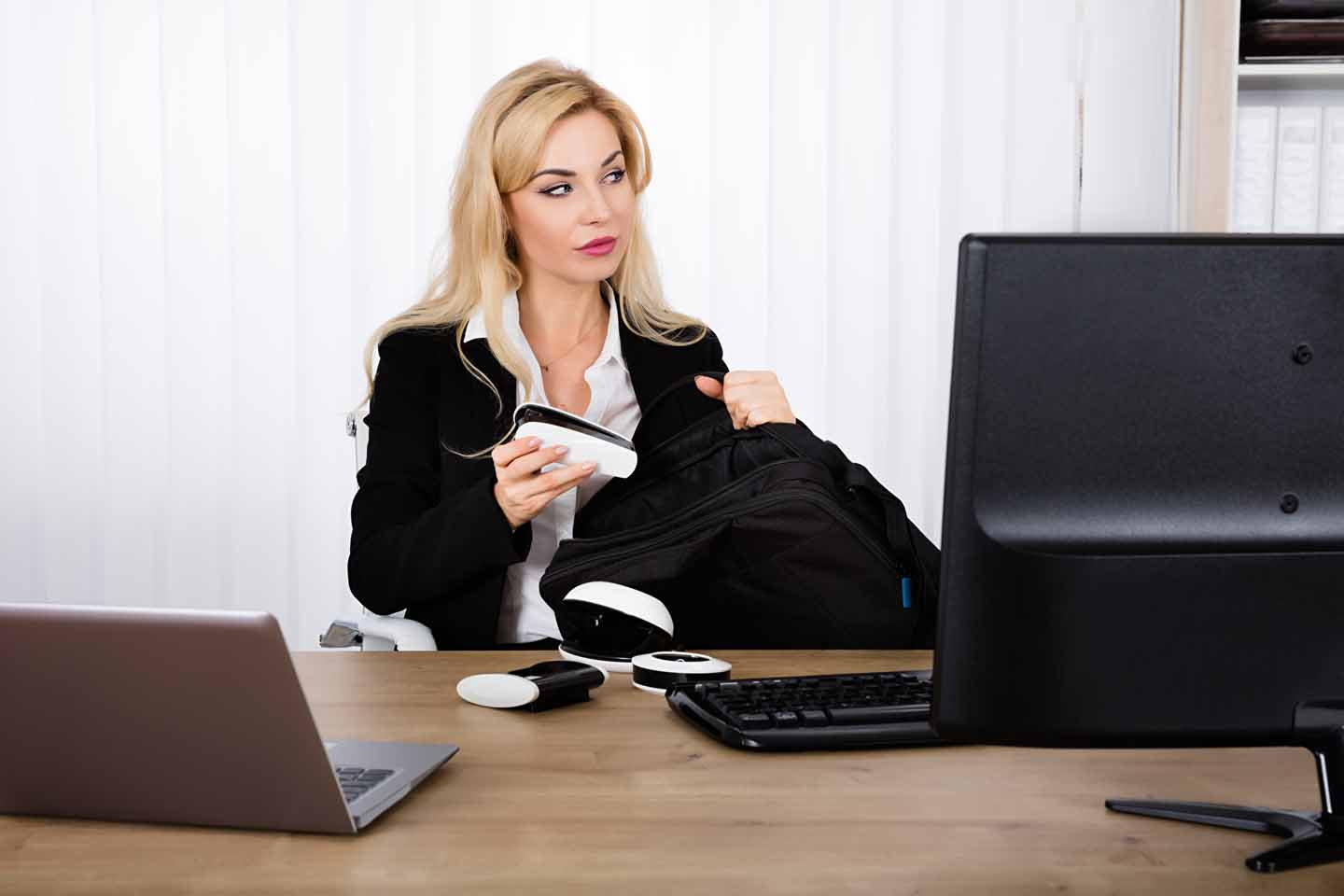 Eine Frau am Arbeitsplatz steckt Büromaterialien in ihre Tasche.