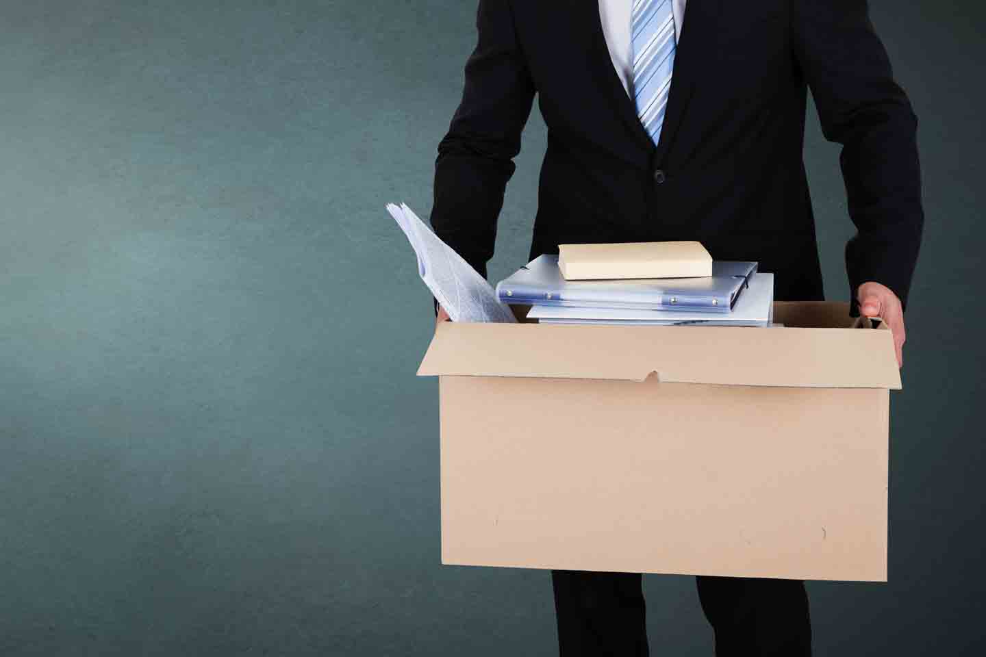 Ein Mann in Anzug trägt einen Karton mit Büromaterialien.