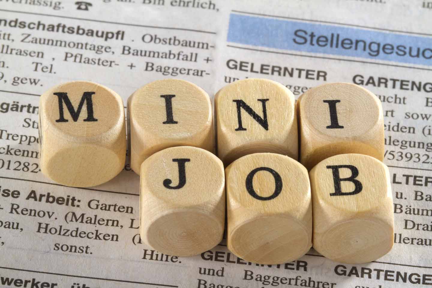 Auf einer Zeitung mit Jobangeboten liegen mehrere Würfel, auf denen Mini Job steht.