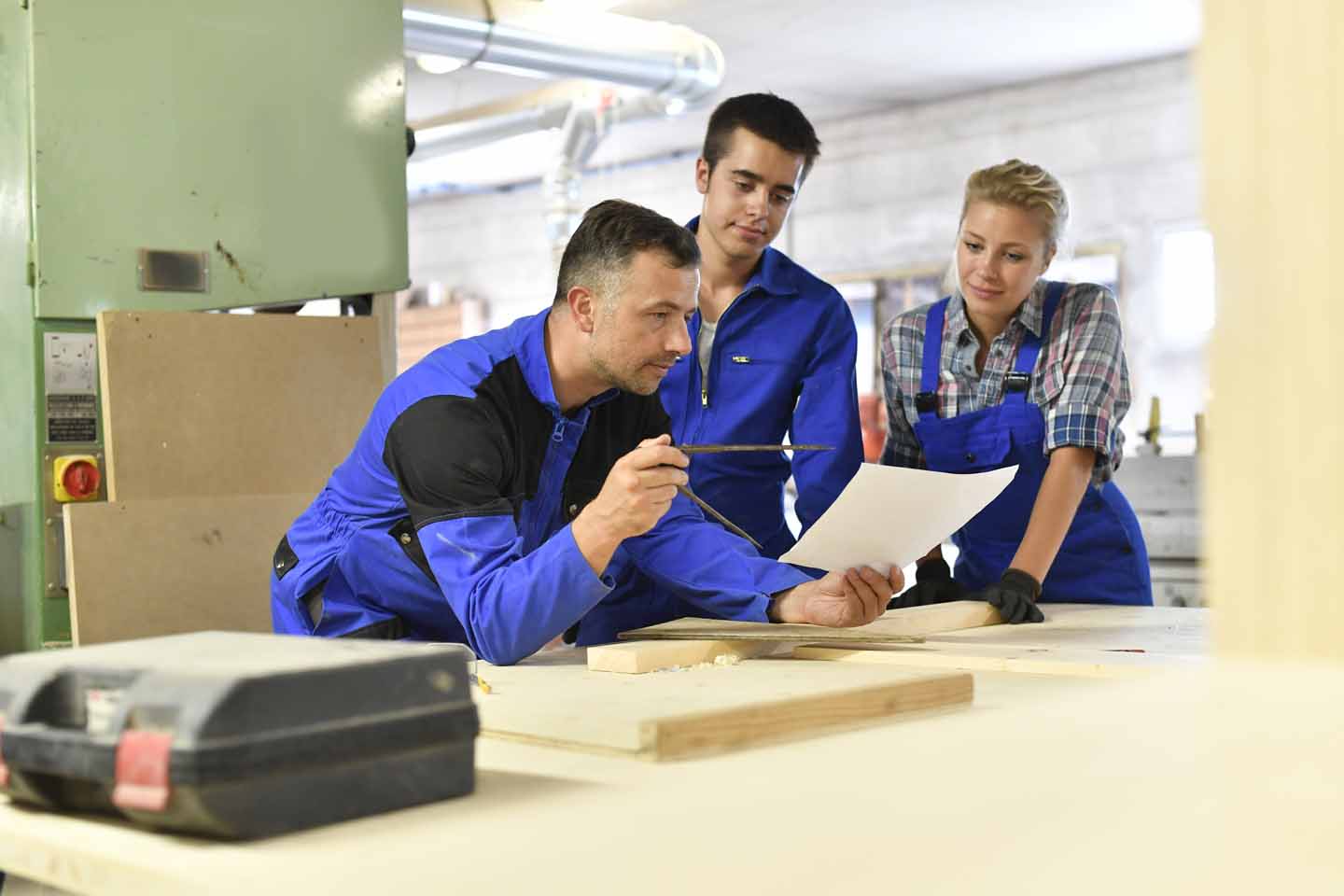 In der Schreinerei: Ein Meister zeigt den Lehrlingen in der Werkstatt Pläne. 