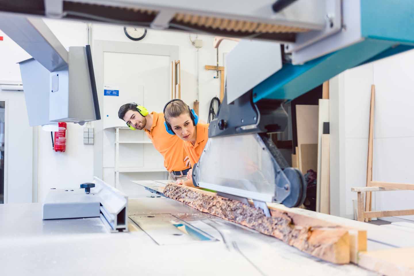 Ein Mann und eine Frau schneien zusammen Holzbohlen in einer Werkstatt zurecht. 