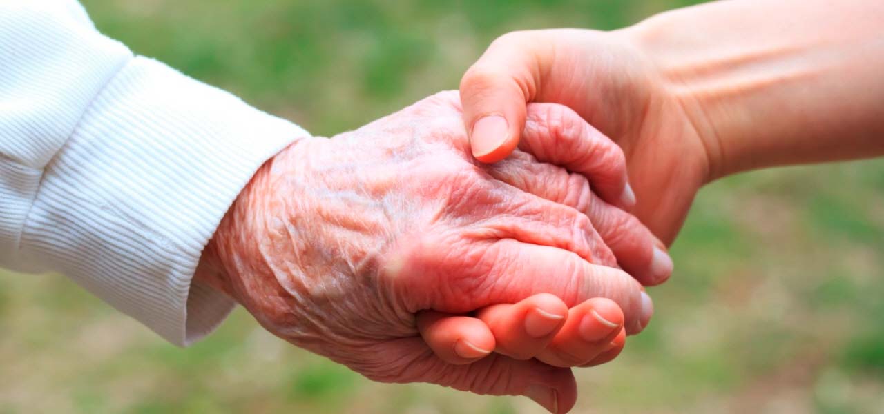 Eine vom Leben gezeichnete, faltige Hand liegt in einer jungen starken Hand.