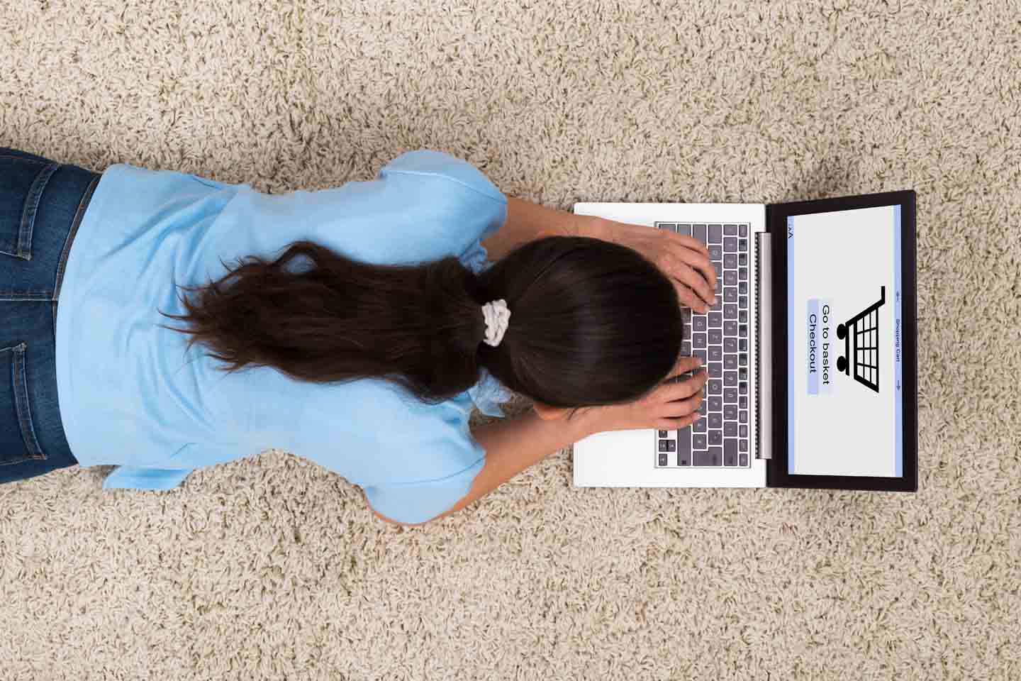 Eine Frau liegt auf dem Boden und shoppt online am Laptop.