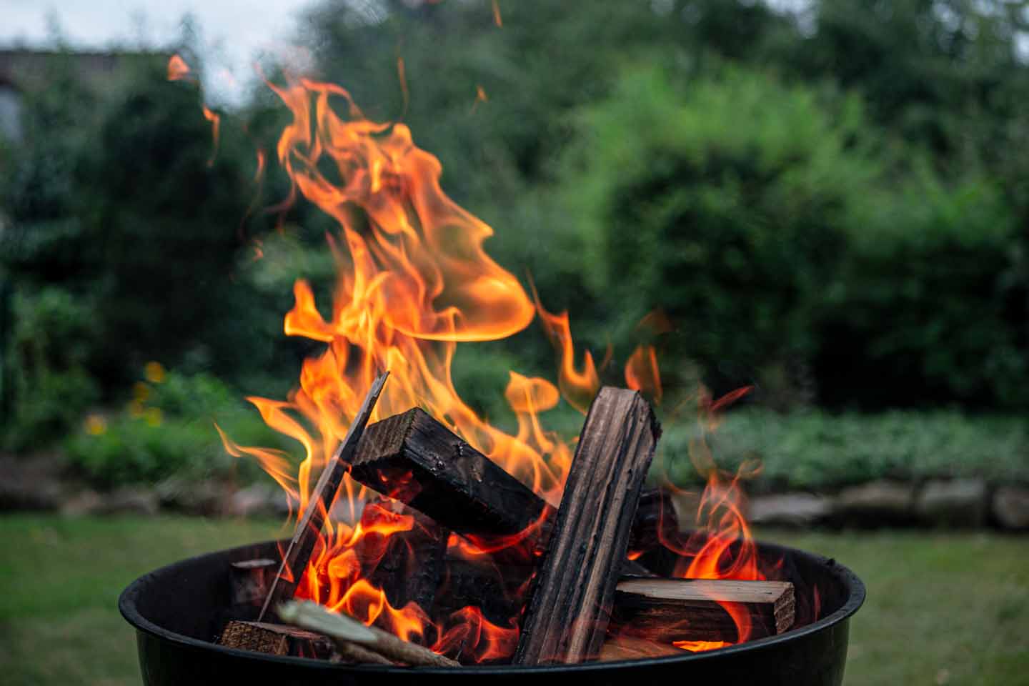 Eine Feuerschale steht im Garten. Die Holzscheite brennen schön gleichmäßig.