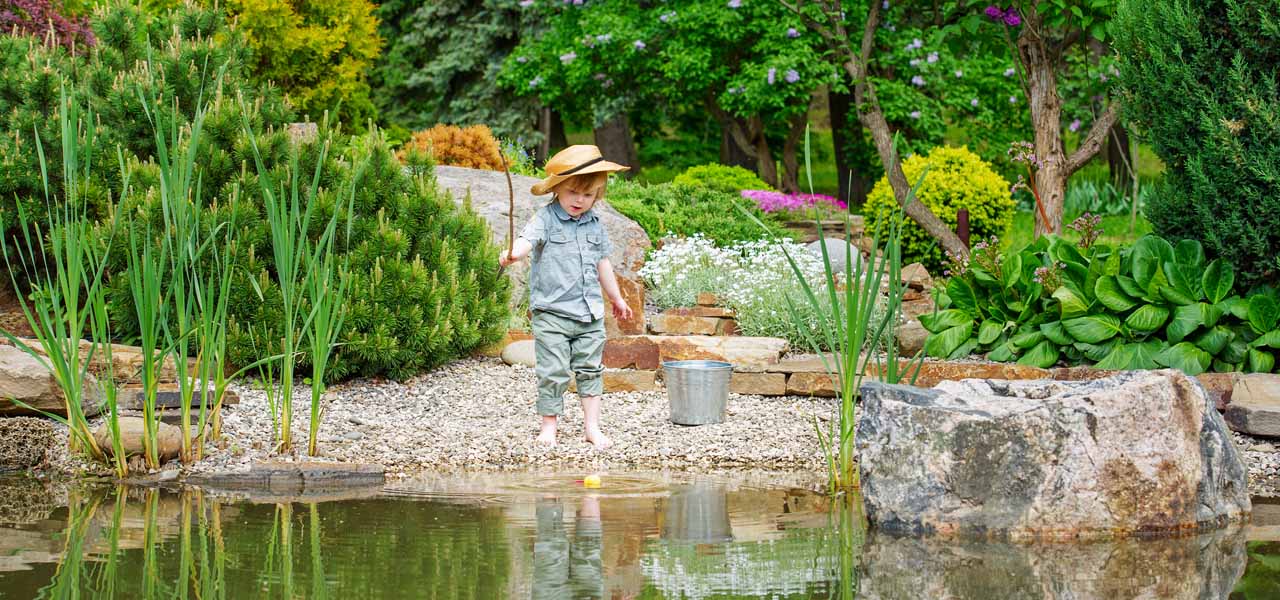 Ein kleines Kind steht an einem ordentlich angelegten Teich.