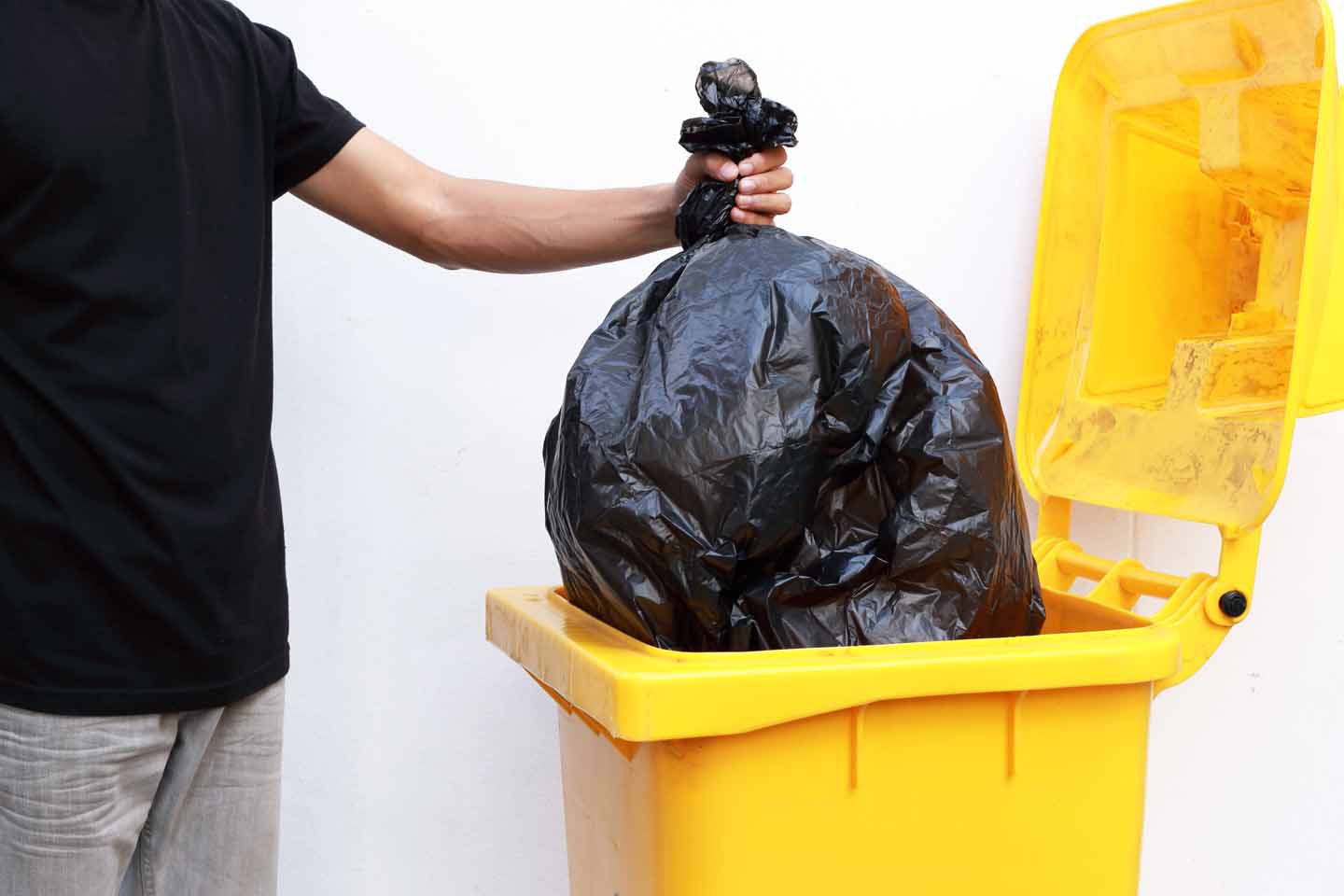 Ein Müllbeutel wird in eine Mülltonne geworfen.