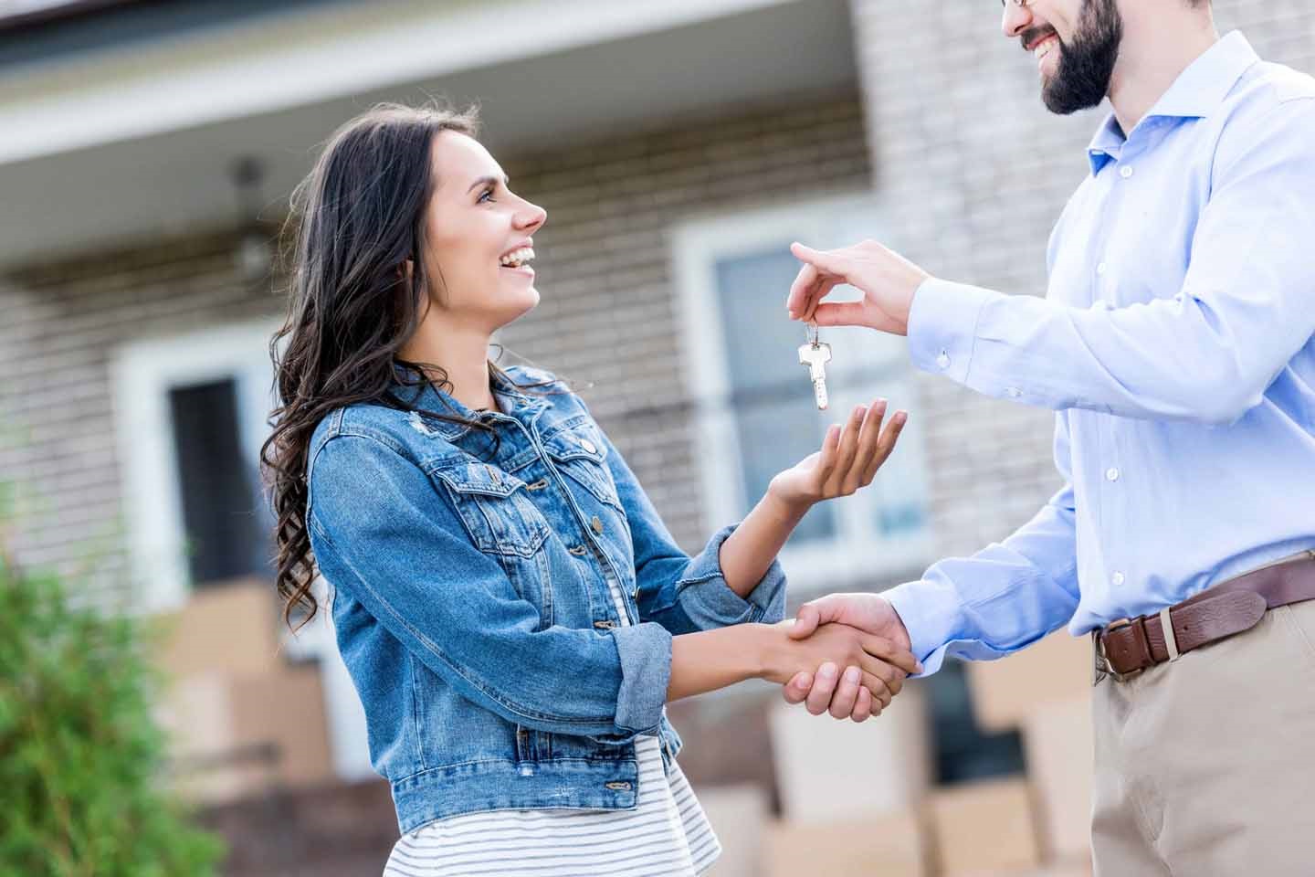 Ein Mann übergibt einer lächelnden Frau einen Hausschlüssel.