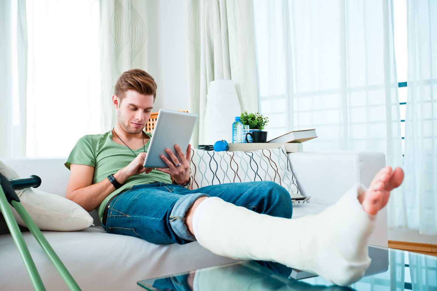 Ein Mann hat sein Gipsbein auf dem Sofatisch liegen und sieht ins Tablet.